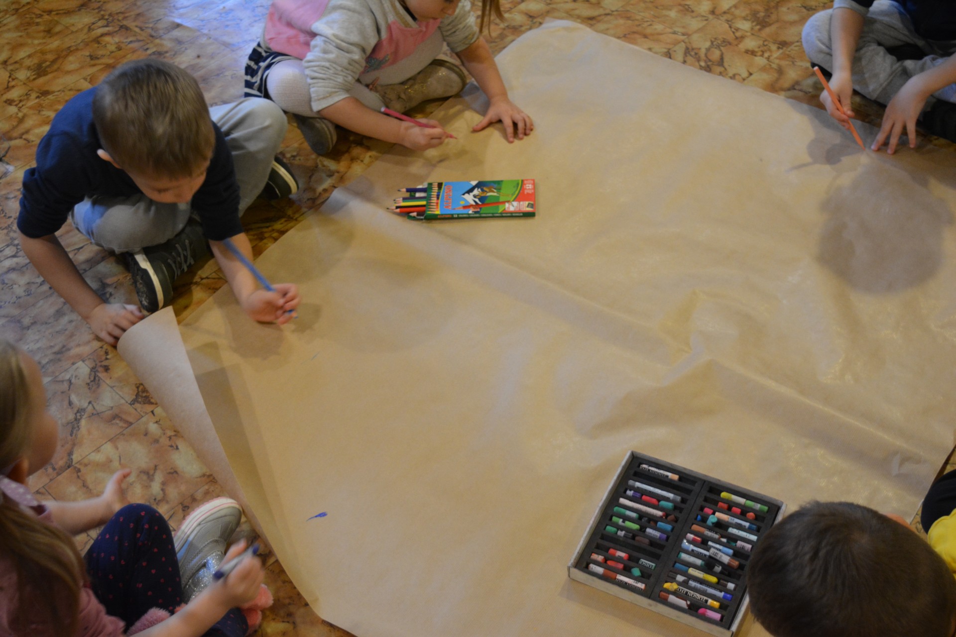 Dzieci rysują w trakcie warsztatów na szarym papierze kredkami różne kształty