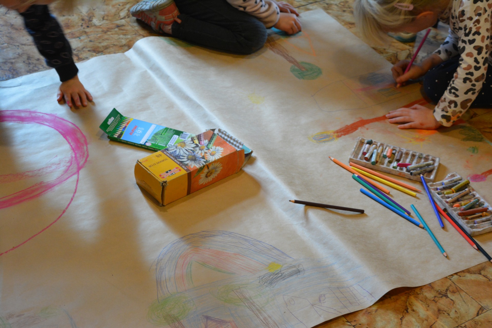 Dzieci rysują w trakcie warsztatów na szarym papierze kredkami różne kształty