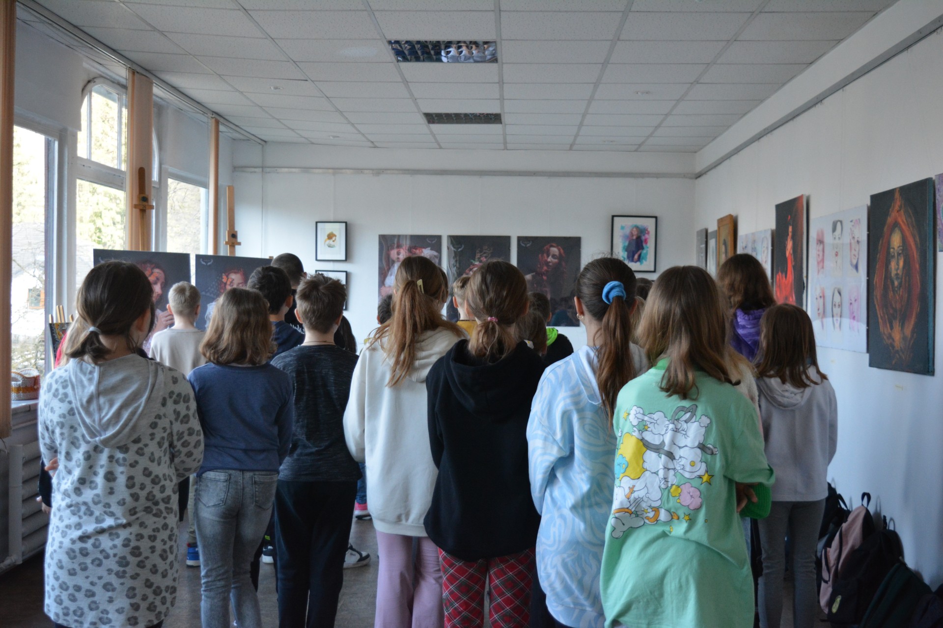 Grupa uczniów zwiedza wystawę prac plastycznych.